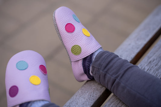 Lilac soft-soled leather shoes with colorful dot details on a child’s feet